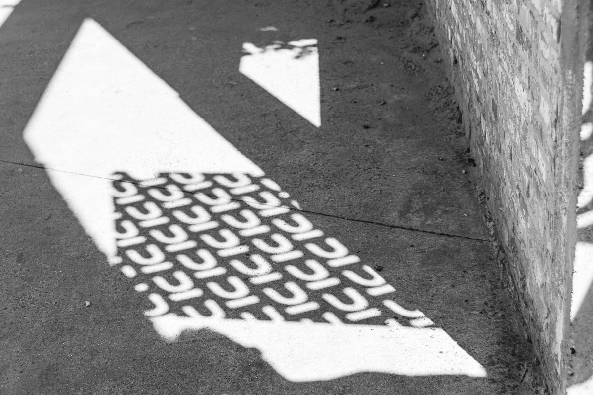 Black and white abstract arrow pointing left on a sidewalk, with a repeating pattern texture, Nuans law firm visual identity