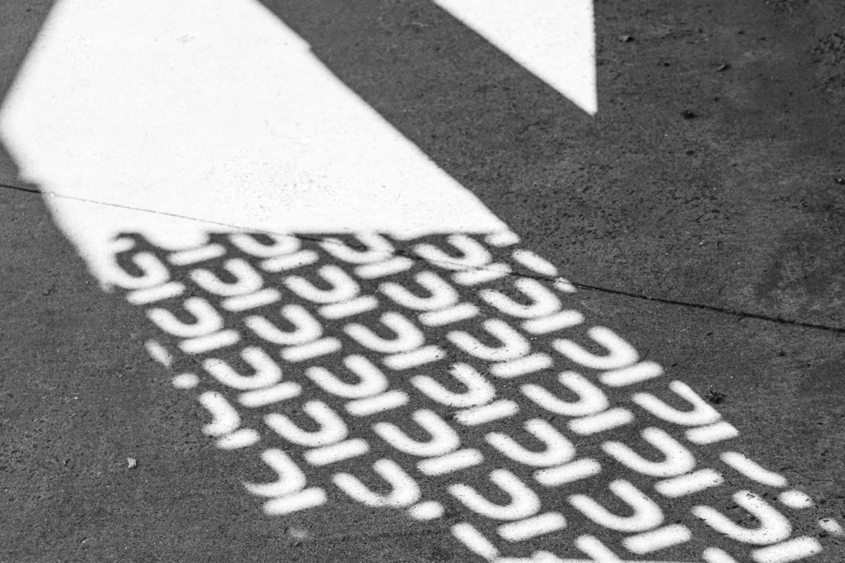 Close-up of white arrow and repeating U-shaped pattern stenciled on asphalt, abstract brand imagery for Nuans law firm
