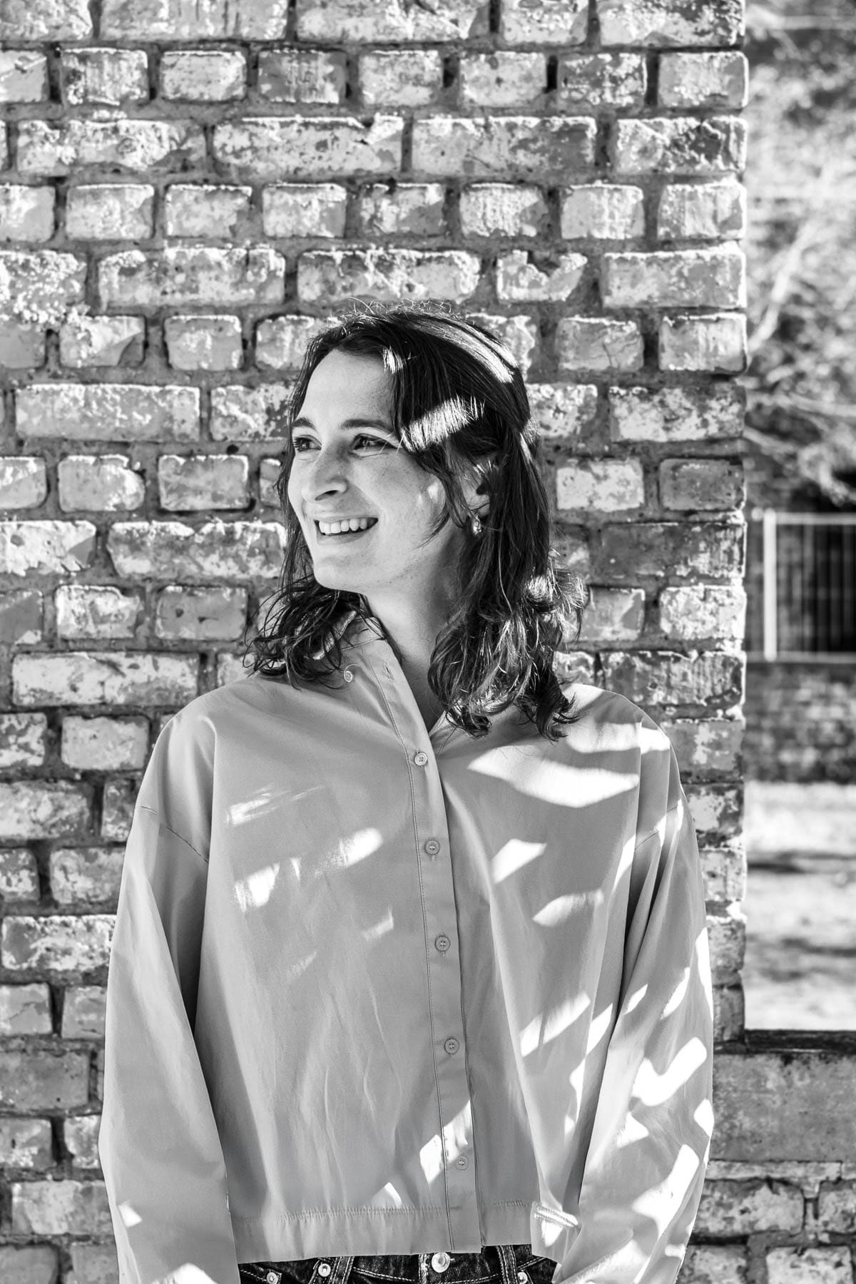 Delphine Hallaert, Associate Innovation lawyer at Nuans, smiling outdoors against a rustic brick wall in black and white port