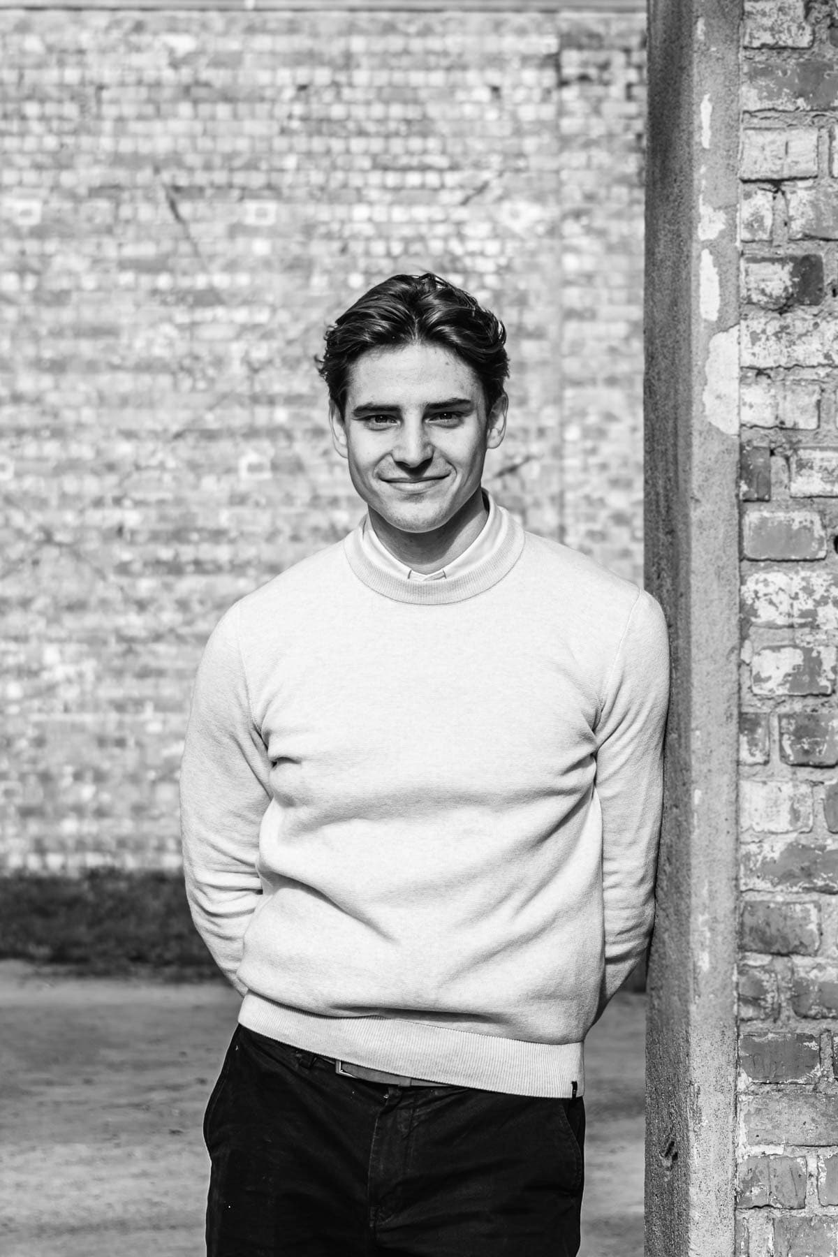 Black and white portrait of Dave Lefevre, lawyer at Nuans specialising in corporate law and M&A, leaning against a brick wall