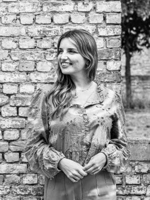 Ellen Caen, team member at Nuans law firm, smiling in a black and white portrait photo outdoors against a brick wall